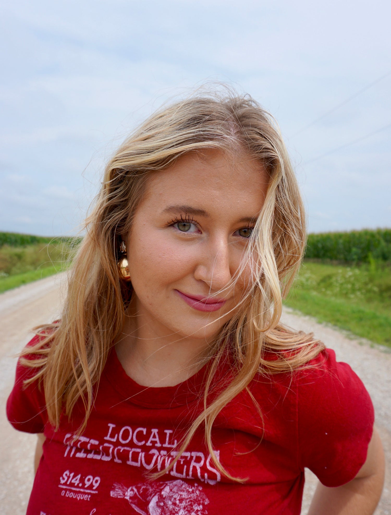 Woman wearing a red t-shirt with text standing on a road with greenery in the background
